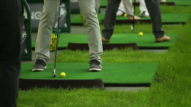 People have training on the golf driving range. Legs and clubs close shot.