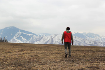 lonely man in red waistcoat walking toward mountains background