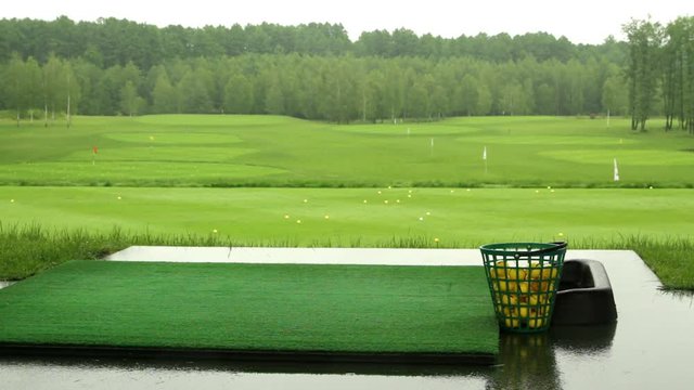 Bucket with yellow golf balls on the driving range in rainy day (wide angle shot).