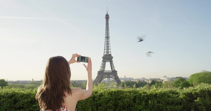 Tourist woman taking photograph of Eiffel Tower using smartphone at sunrise photographing scenic Paris cityscape background view enjoying European honeymoon vacation travel adventure