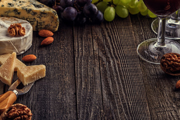 Cheese, nuts, grapes and red wine on wooden background.