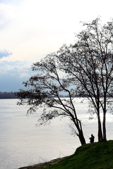 Silhouette of fisherman with fishing rod at cloudy spring in background trees and Danube River
