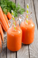 Fresh carrot juice in a bottles on rustic wooden background, selective focus