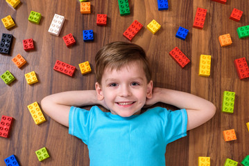 Little caucasian child playing with lots of colorful plastic blocks indoor. Kid boy wearing shirt and having fun building creating © pahis