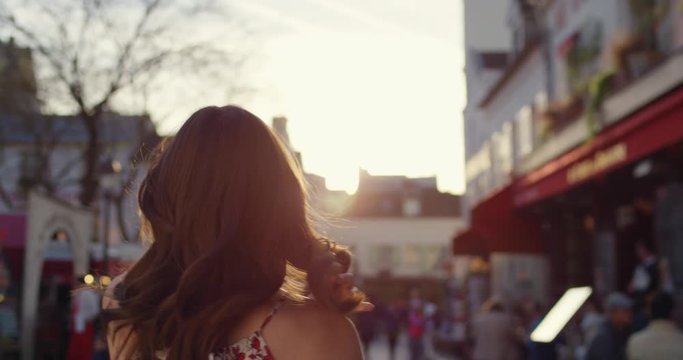 Rear view woman walking through European street at sunset wearing pretty floral summer dress sunshine lens flare confident girl exploring local Paris enjoying holiday travel vacation adventure