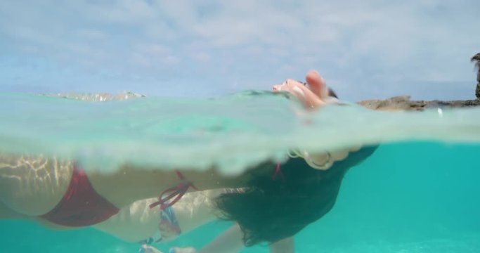 Woman floating in ocean wearing red bikini diving down in clear blue tropical water on summer beach vacation