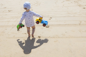 Fototapeta premium Baby boy walking with toys at the beach