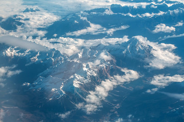 Naklejka na ściany i meble Idyllic snowy mountain peaks under clouds from plane