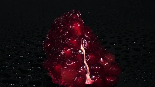 Breathtaking view of pomegranate seeds rotating over black background and spraying by water. Macro eye shot. Sweet tasty fruit looks like brilliant jewels. Luxury healthy food concept in 4K
