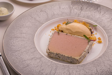 Parfait from a liver of a guinea fowl served on a big round plate with black truffle and ice cream