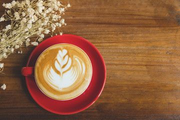 A red cup of coffee with vintage flower on wood table in coffee shop