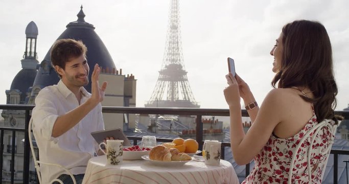 Young tourist couple in Paris hotel enjoying breakfast on terrace Woman taking holiday photo of husband on honeymoon view of Eiffel Tower at Sunrise in the morning