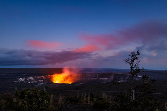 The fiery glow of the lava lake of Kilauea's active crater of Halemaumau illuminates pink clouds at the blue hour. View from Jaggar museum, Volcanoes National Park, Big Island, Hawaii.