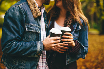 Happy young couple with coffee cups walking in autumn park