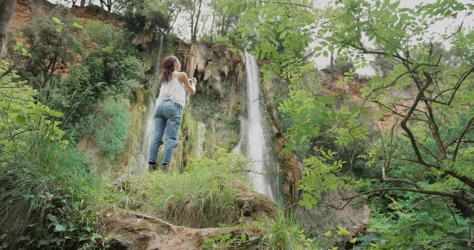 Young woman taking photograph with smart phone at base of hidden waterfall girls in nature enjoying carefree vacation outdoors adventure