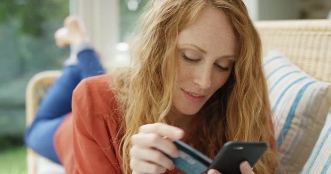 Online shopping Close up of beautiful red haired woman holding credit card making payment using smartphone at home in trendy loft apartment 