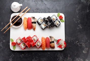 Japanese cuisine. Sushi set on a white plate over dark stone background.