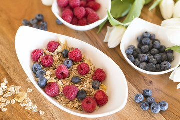 Breakfast with granola or muesli und fresh raspberries and blueberries on a wood table 