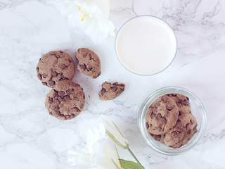 Crisp chocolate cookies with a glass of milk and white flower on marble background. Flat lay. Top view