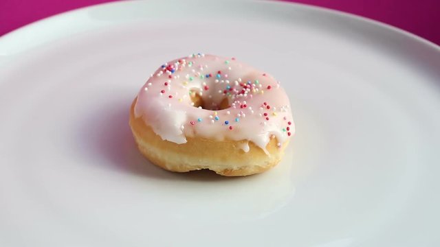 rotating donut with colorful toppings on pink background
