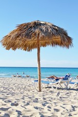 Fototapeta na wymiar Straw roof of beach umbrella and blue sky on white sandy beach with ocean in background