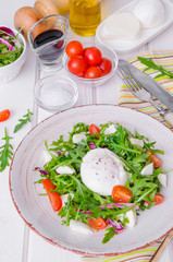 Fresh salad with arugula, mozzarella, cherry tomatoes and poached egg