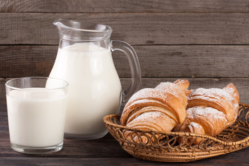 jug and glass of milk with croissants on a wooden background