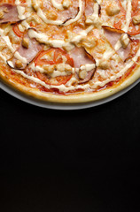 Pizza with chicken and vegetables on a white plate and a black table