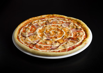 Pizza with chicken and vegetables on a white plate and a black table