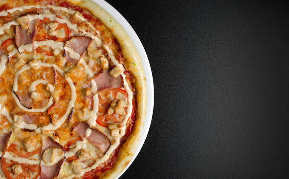 Pizza with chicken and vegetables on a white plate and a black table