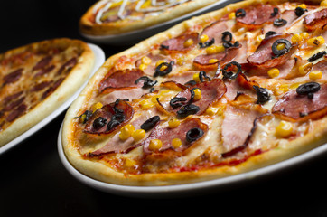 Three different pizzas on a white plate and a black table