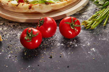 Whole and cutted tomato in ingredients of pizza on italian black paper table