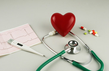 Stethoscope, electrocardiogram, thermometer, and a red heart on a gray background.