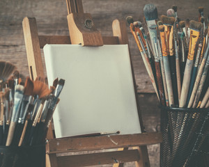 Artistic equipment: empty artist canvas on easel and paint brushes in a artist studio. Retro toned...