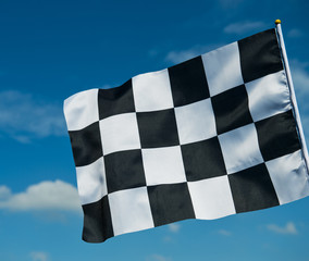 checkered race flag waving on blue sky.