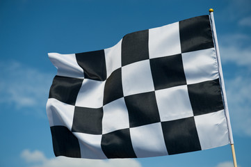 checkered race flag waving on blue sky.