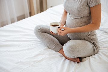 Fototapeta na wymiar Pregnant woman sitting on bed and drinking coffee at home