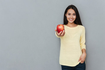 Happy cute young woman standing and giving you red apple