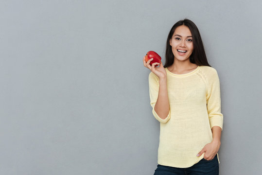 Smiling pretty young woman standing and holding red apple