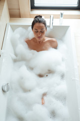 Peaceful young woman with closed eyes relaxing in bathtub
