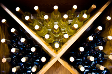 Group of red wine bottles stacked on wooden racks.