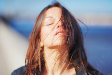 Gorgeous emotional girl enjoying a Sunny summer day, eyes closed, a face of bright sunlight. The wind ruffled her hair. Blurred background, close-up