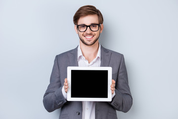 Happy young man in formal wear with smile holds digital tablet and shows copyspace on screen while...