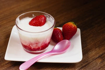 Strawberry flavored tapioca pudding served in glass cup on darkwood table with pink spoon and some fresh strawberries
