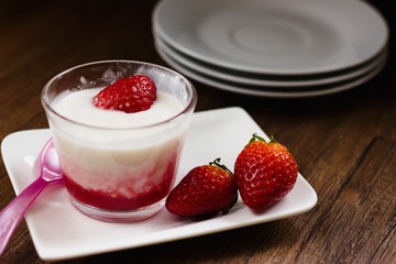 Strawberry flavored tapioka pudding in glass cup on dark wood table with strawberries and pink spoon