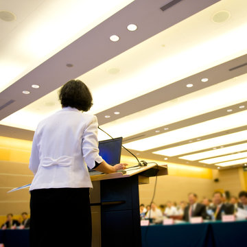Business woman is making a speech in front of a big audience at a conference hall..