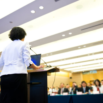 Business woman is making a speech in front of a big audience at a conference hall..