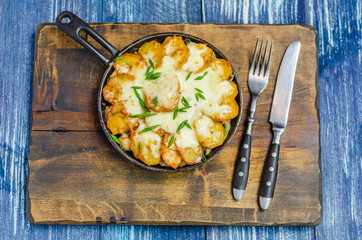 Frying pan with potatoes, cheese and herbs, cutlery