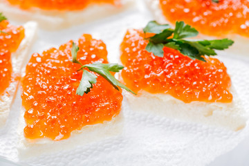 Sandwiches with salmon red caviar and herbs on white napkin. Close up image with selective focus