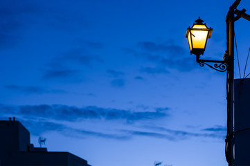 Fototapeta na wymiar Historic street lamp, illumination in the blue hour radiating a warm, soft yellow light.